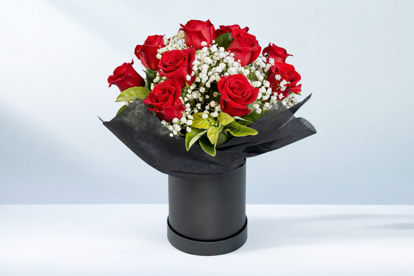 Valentine’s Day arrangement of 12 red roses with baby’s breath and greenery, styled in a black hatbox container, approximately 40cm in length.