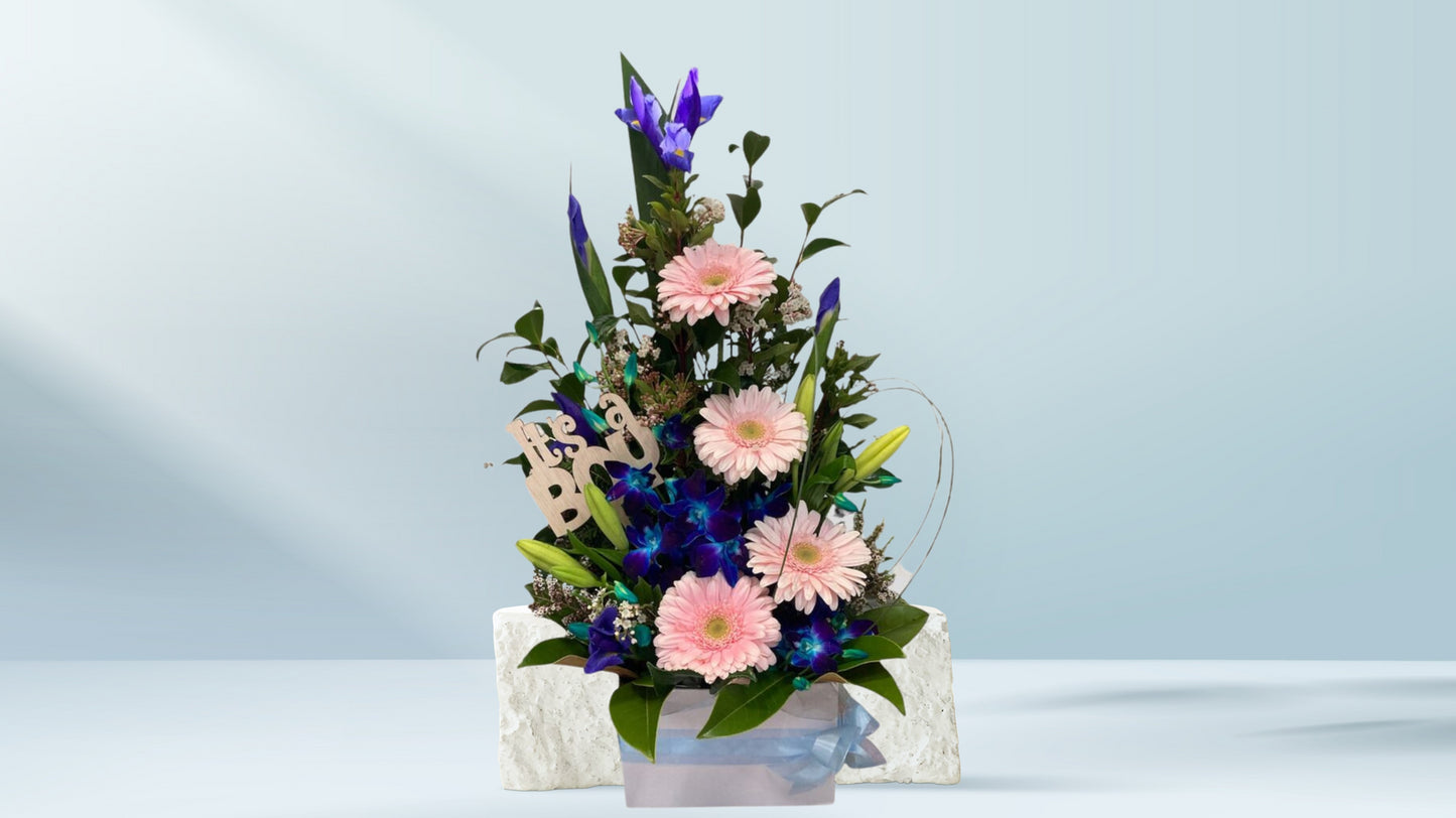 Floral arrangement with pink and purple flowers in a white box on a light blue background