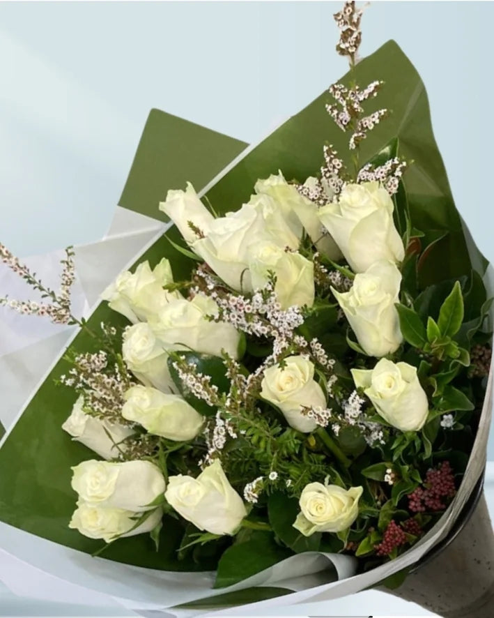 Bouquet of white roses wrapped in green paper with a light blue background
