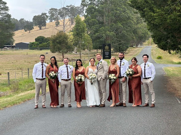 Wedding party posing on a rural road with greenery in the background showing flowers from emflowerment