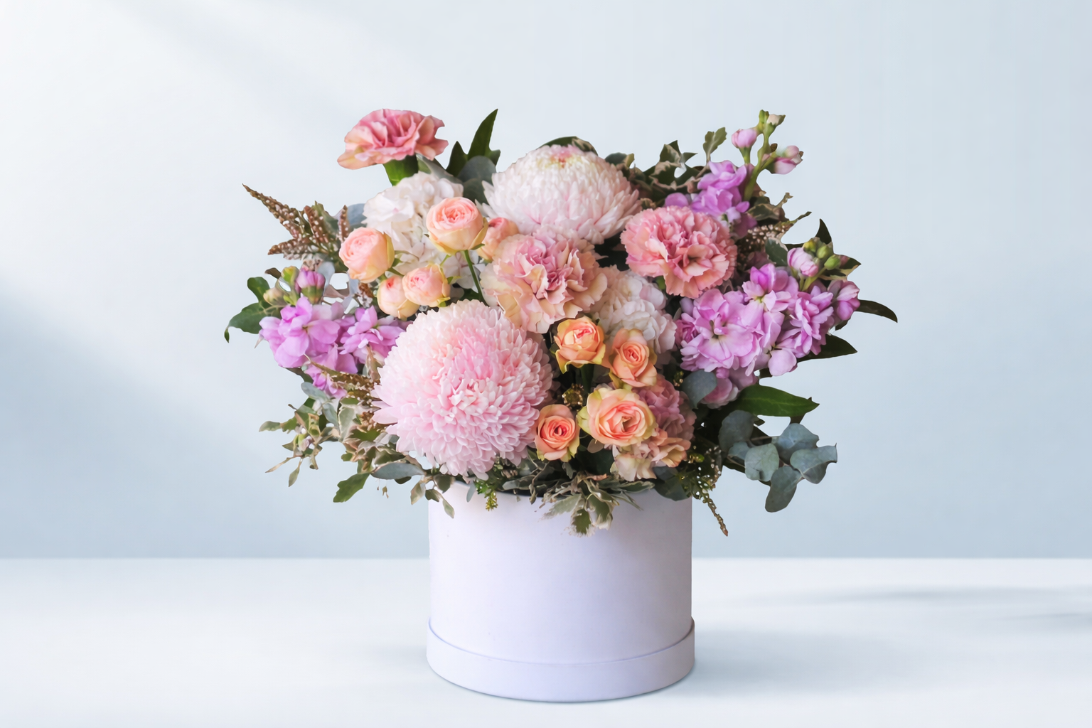 Elegant pastel flower arrangement in a white hatbox featuring pink disbuds, roses, carnations and stock, styled by Emflowerment Florist in Croydon with delivery available across Melbourne.