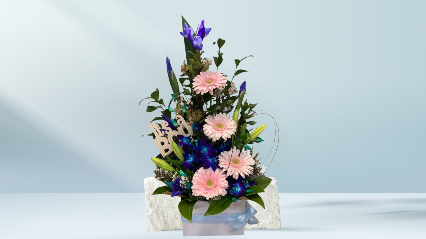 Floral arrangement with pink and purple flowers in a white box on a light blue background