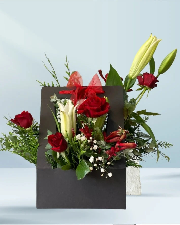 Floral arrangement with red roses and greenery in a black box on a light blue background