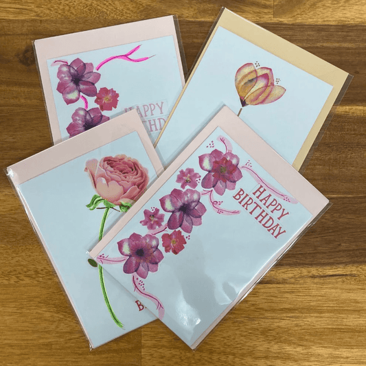 Four birthday cards with floral designs on a wooden surface