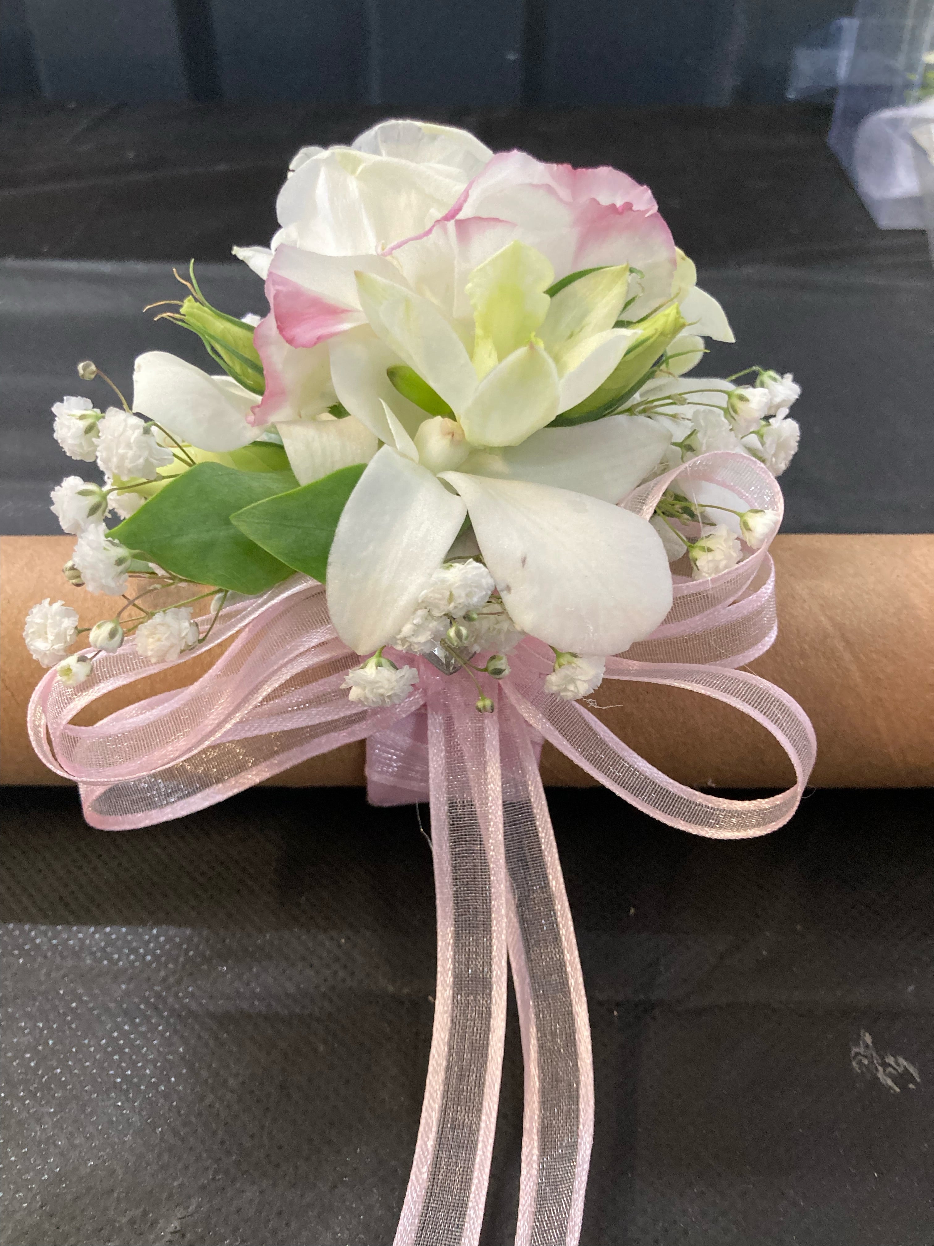 White and pink wrist corsage with orchids and baby’s breath, finished with a soft pink ribbon.