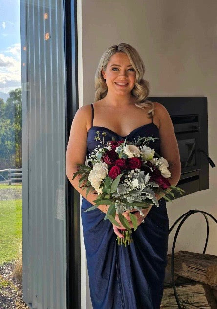 Kimberley in a blue dress holding a bouquet of flowers indoors for a wedding