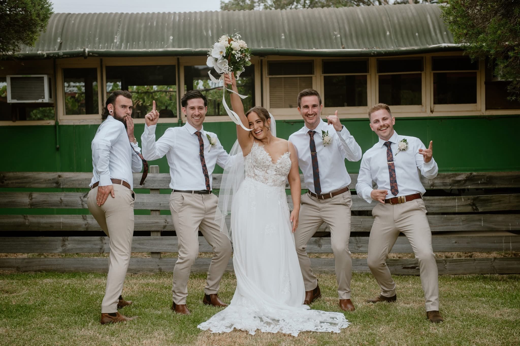 Wedding party celebrating outdoors with a bride holding a bouquet in front of a building.