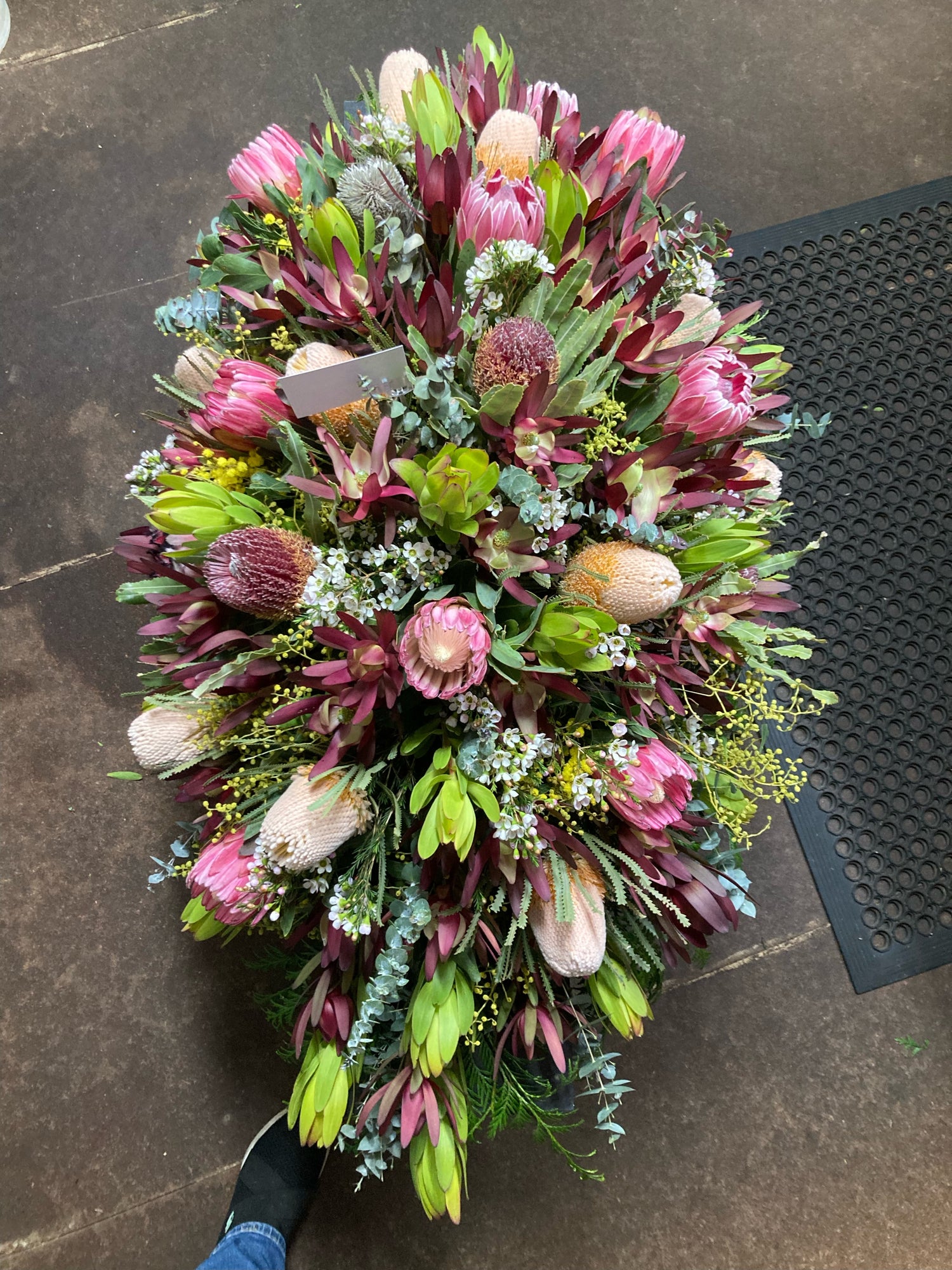 Native Australian funeral flower arrangement featuring proteas, leucadendrons, eucalyptus and mixed greenery, created by Emflowerment Florist Croydon for sympathy and memorial services.