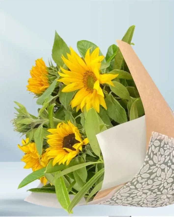 Bouquet of sunflowers wrapped in white paper with a light blue background
